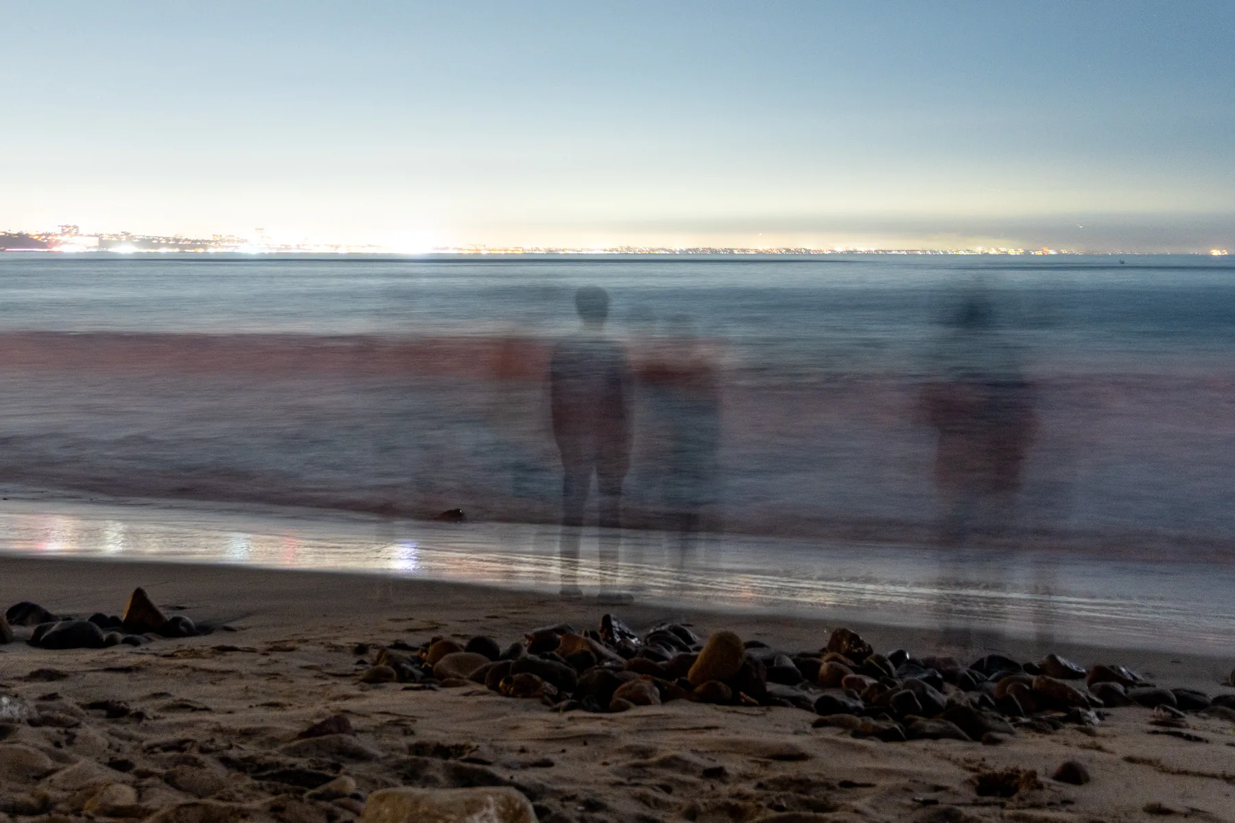 Long-exposure figures standing along a moonlit shoreline